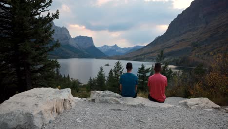 Glacier-National-Park,-Montana-USA---Zeitraffer-Mit-2-Personen,-Die-Auf-Einem-Felsen-Sitzen,-Während-Die-Wolken-Und-Touristen-Kommen,-Um-St.-Mary-Lake-Und-Wild-Good-Island-Zu-Fotografieren