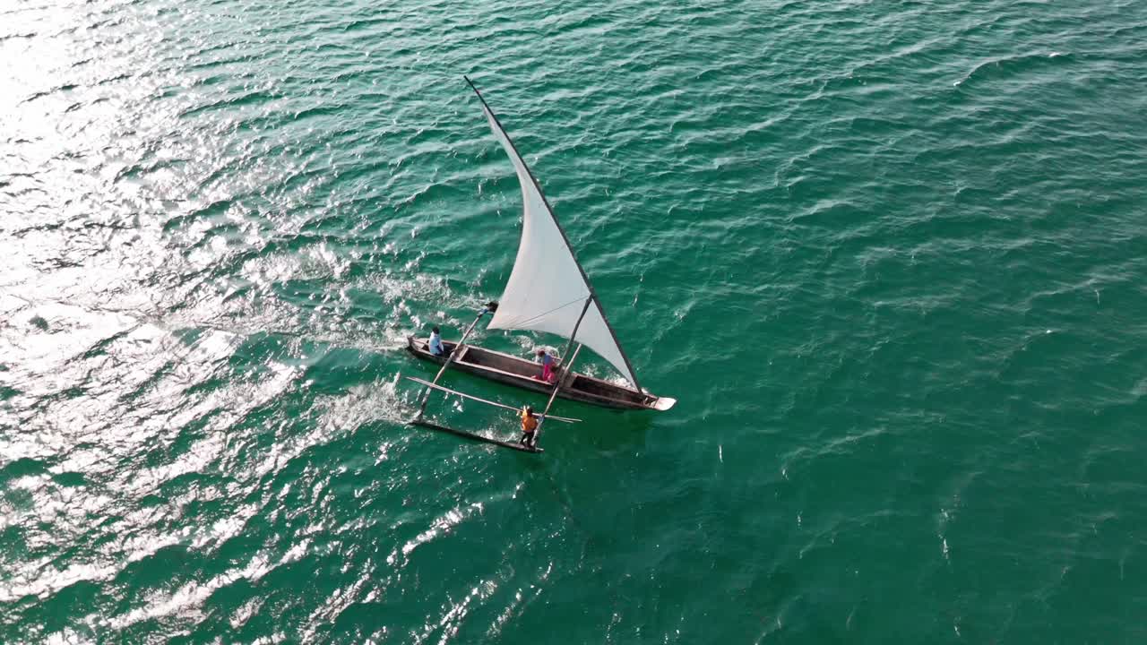 A small sailboat glides over turquoise ocean waters under a clear sky