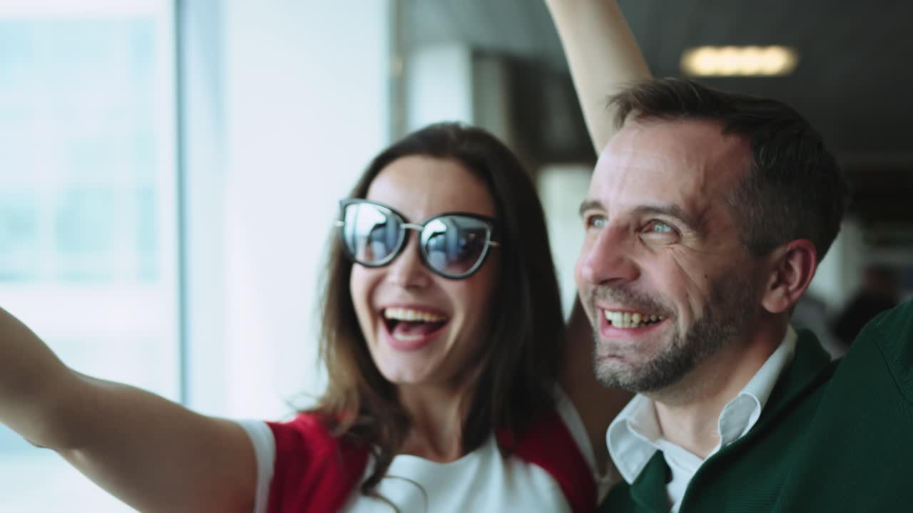 giovane coppia bellissima nella sala dell'aeroporto. donna bruna sorridente e uomo che scattano una foto selfie sullo smartphone vicino alla finestra. colpo cinematografico sulla telecamera rossa. 2 modelli.