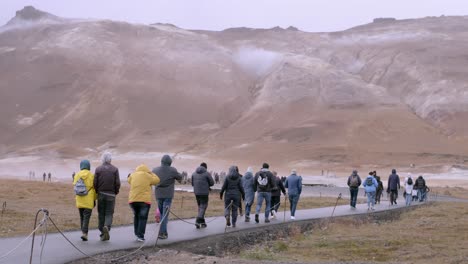 tourists in warm clothing walk towards iceland's steaming namaskaro hot springs on a cloudy day