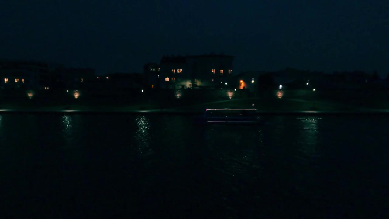 夜になると、川沿いの建物から漏れる光が水面に反射します。穏やかな水面は、暗い周囲の景色と遠くの水平線を静かに映し出します。