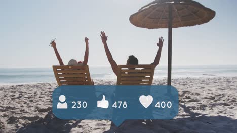 Animation-of-people,-thumbs-up-and-heart-icons-and-numbers-over-couple-in-deckchairs-on-beach