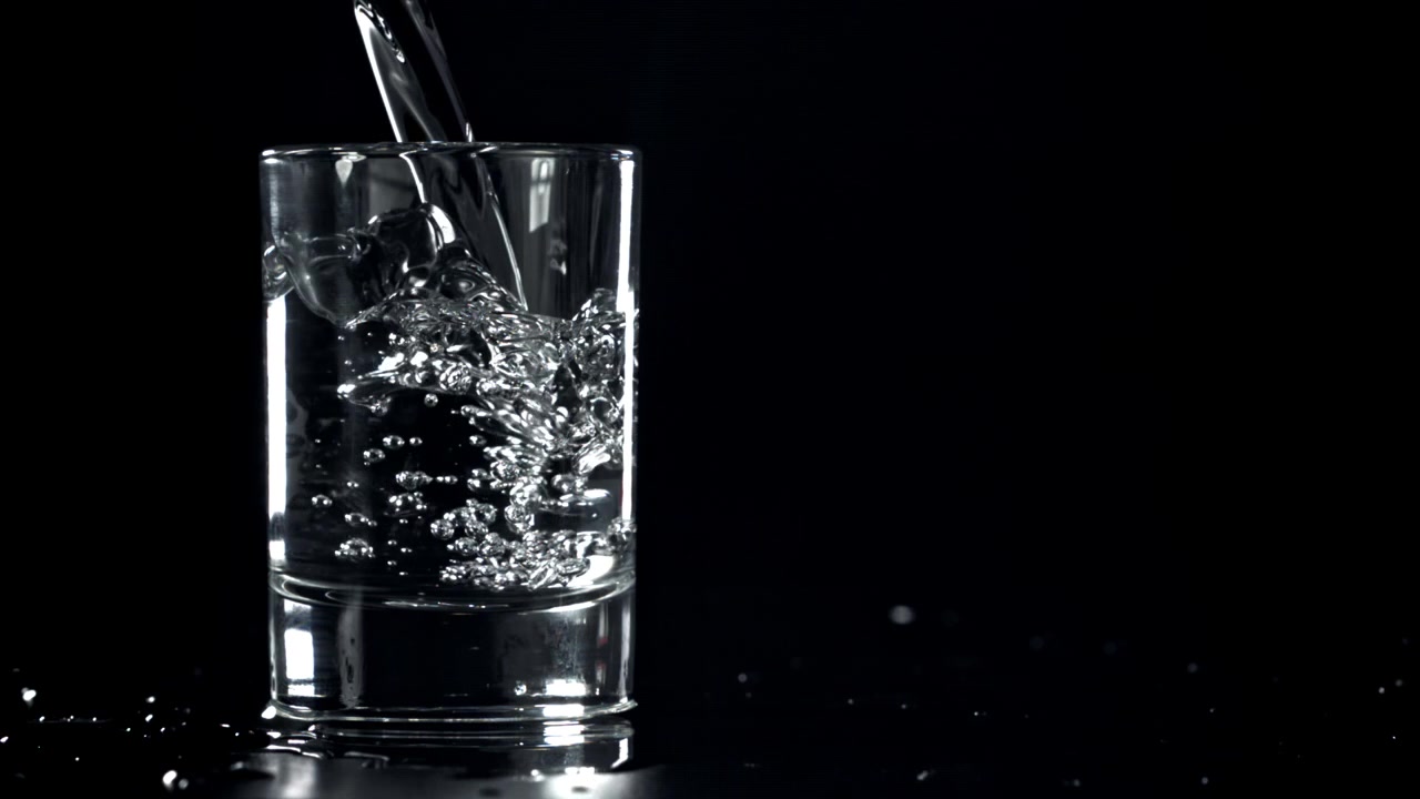 Slowmotion af vand, der hældes i et klart glas på sort baggrund