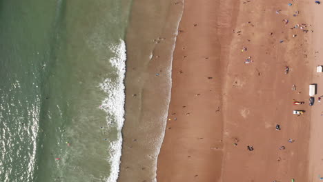 aerial flyover of a golden sandy beach in north devon with people sunbathing and a truck driving down the beach