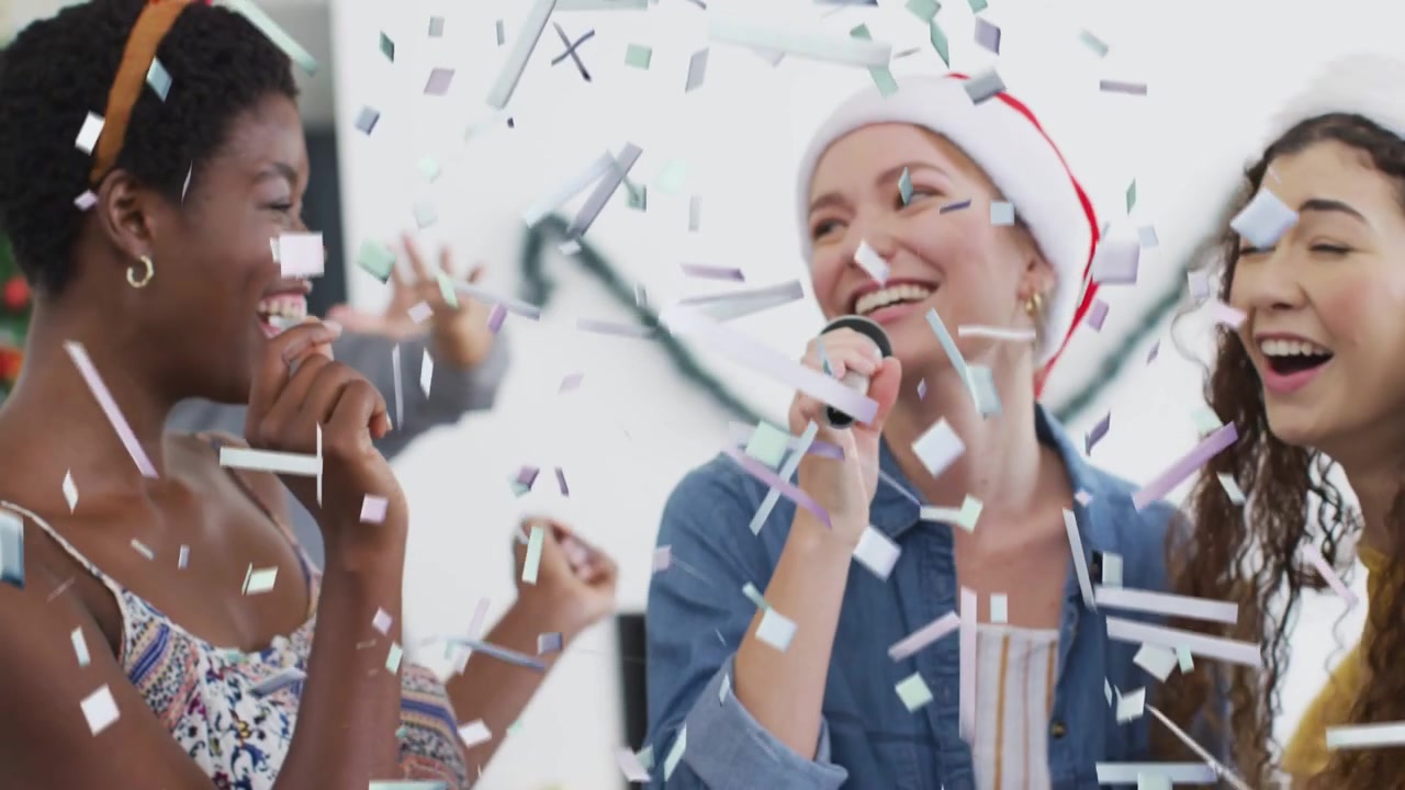 Barstende confetti begint feestvreugde, drie vrouwen delen microfoon, zingend, harmoniserend, klappend.