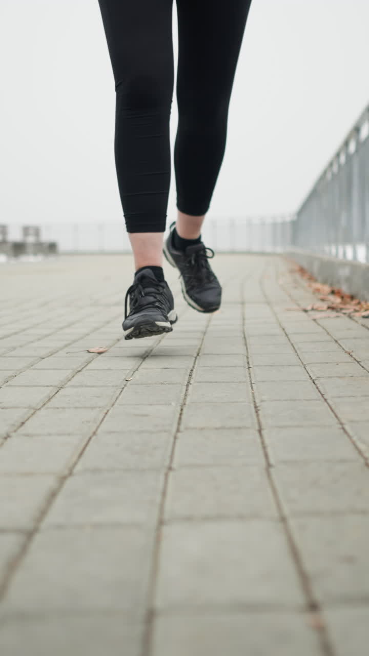 Leg view of athlete wearing black sneakers jogging along snowy pathway near iron railing under foggy sky with serene mood and decorative structure benches faintly visible in background