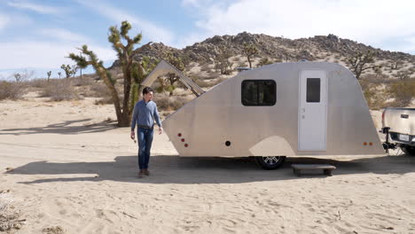 slow motion shot of a handsome man in the desert on a camping trip in a metal teardrop travel trailer and tiny house