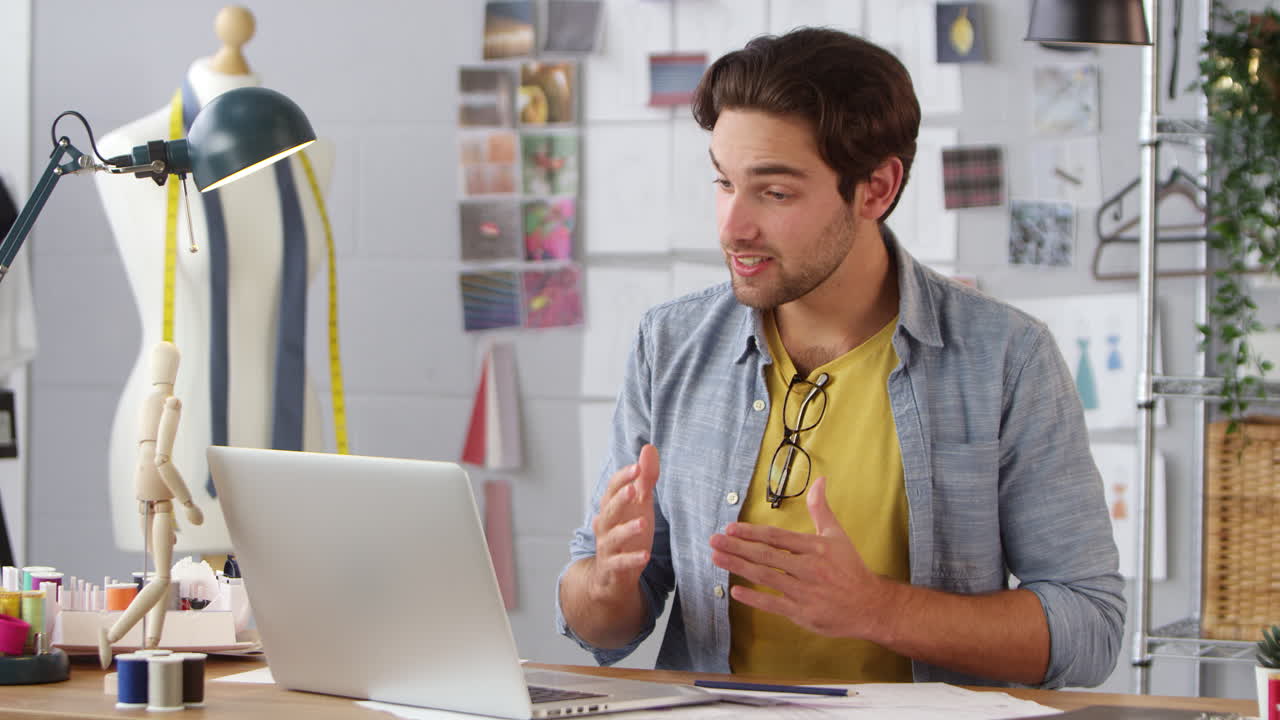 Male Business Owner Working In Fashion Showing Designs On Video Call Using Laptop