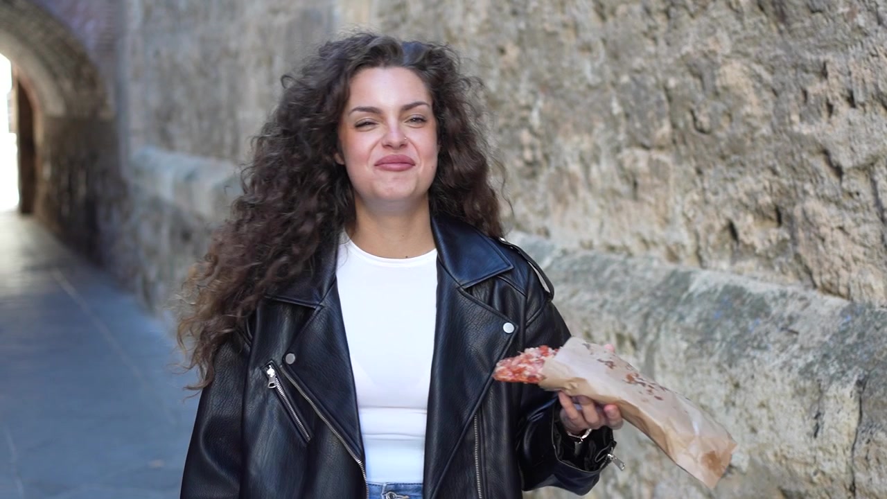 This is a portrait featuring a woman confidently holding a fish while standing in an urban alleyway