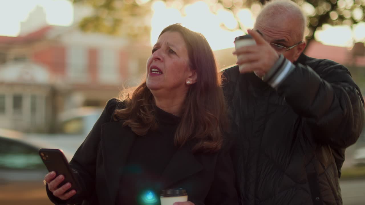 Mature Couple Navigating or Discussing Outdoors with Smartphone and Coffee
