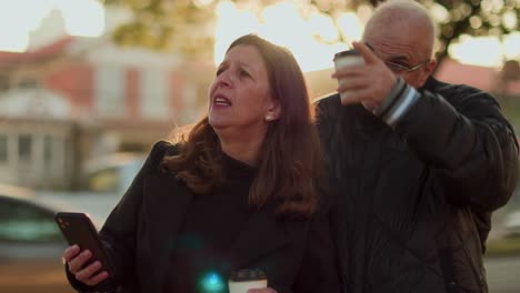 mature couple navigating or discussing outdoors with smartphone and coffee