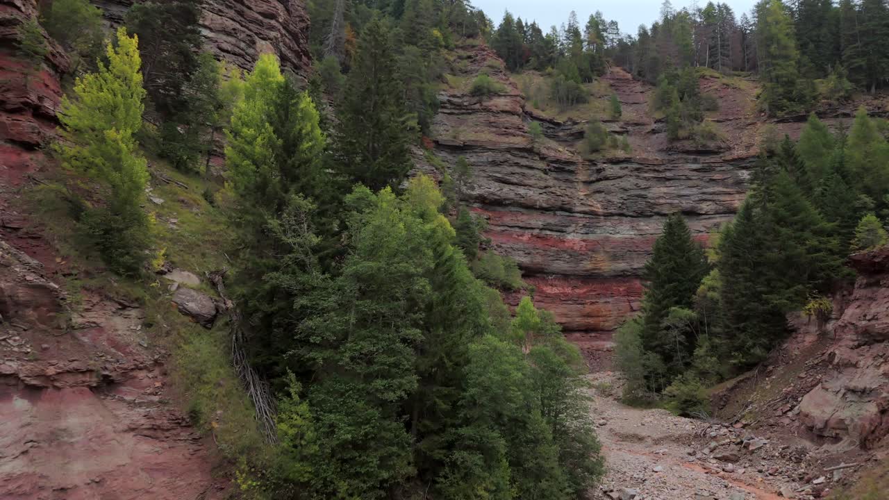Bletterbach Gorge in South Tyrol, Italy, showcasing impressive red and gray rock layers alongside green forest. This rugged natural landscape highlights the region’s unique geological formations.
