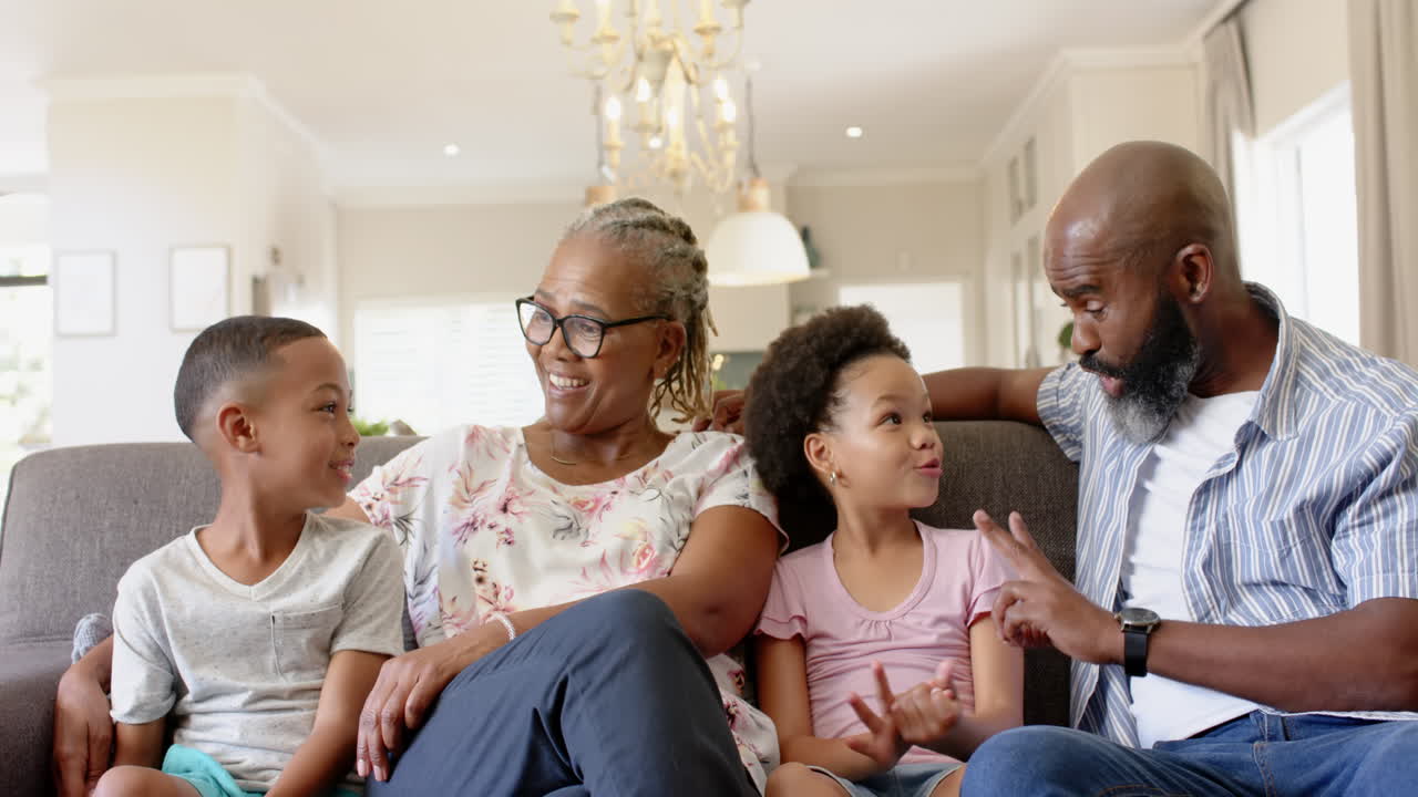 Laughing together, african american grandparents and grandchildren sitting on couch in living room