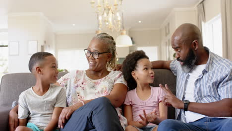 laughing together, african american grandparents and grandchildren sitting on couch in living room
