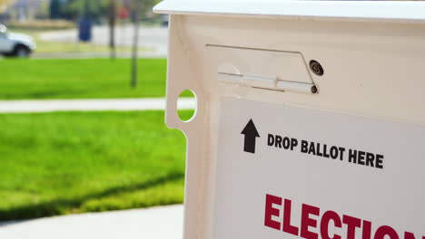 drop ballot here sign with arrow and slot for mail-in election voting box with person walking and car in background