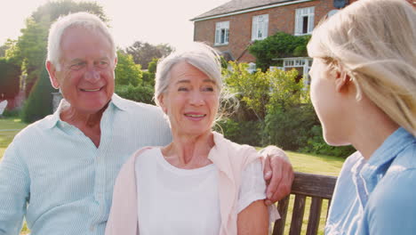 Senior-Parents-Sitting-On-Seat-In-Garden-With-Adult-Daughter