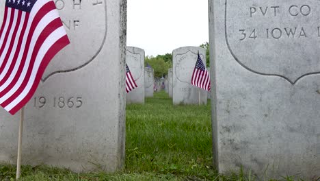 close up view of old white gravestones of veterans in a cemetery on memorial day in a graveyard with american flags