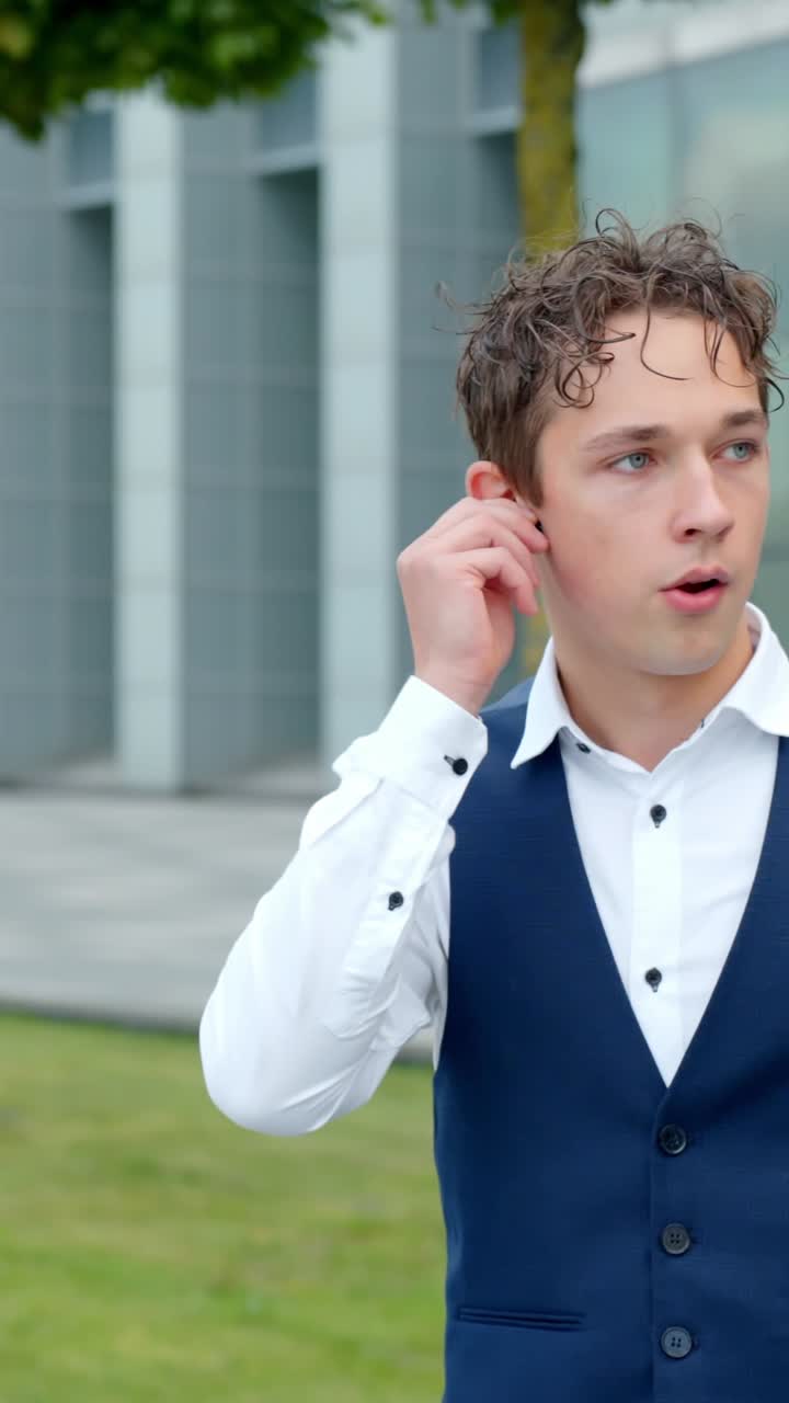 A Young Finance Analyst Walks While Talking Through His Earpiece - Vertical Shot