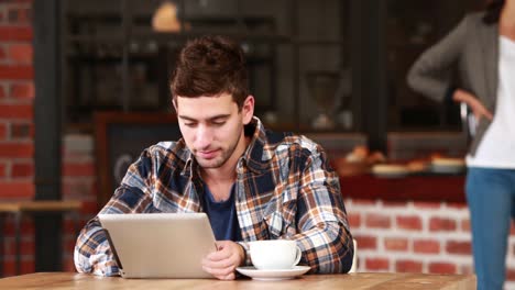 Smiling-hipster-man-using-a-tablet-and-sipping-coffee