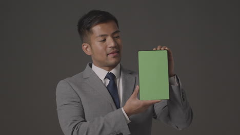 studio shot of smiling businessman in suit holding green screen digital tablet