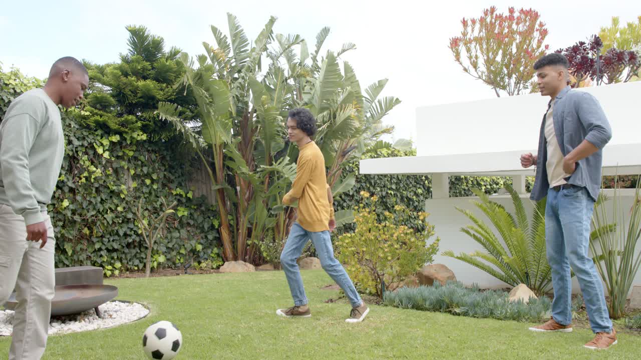Tapping soccer ball lightly, three male friends practicing keep-away drill near fire pit on lawn