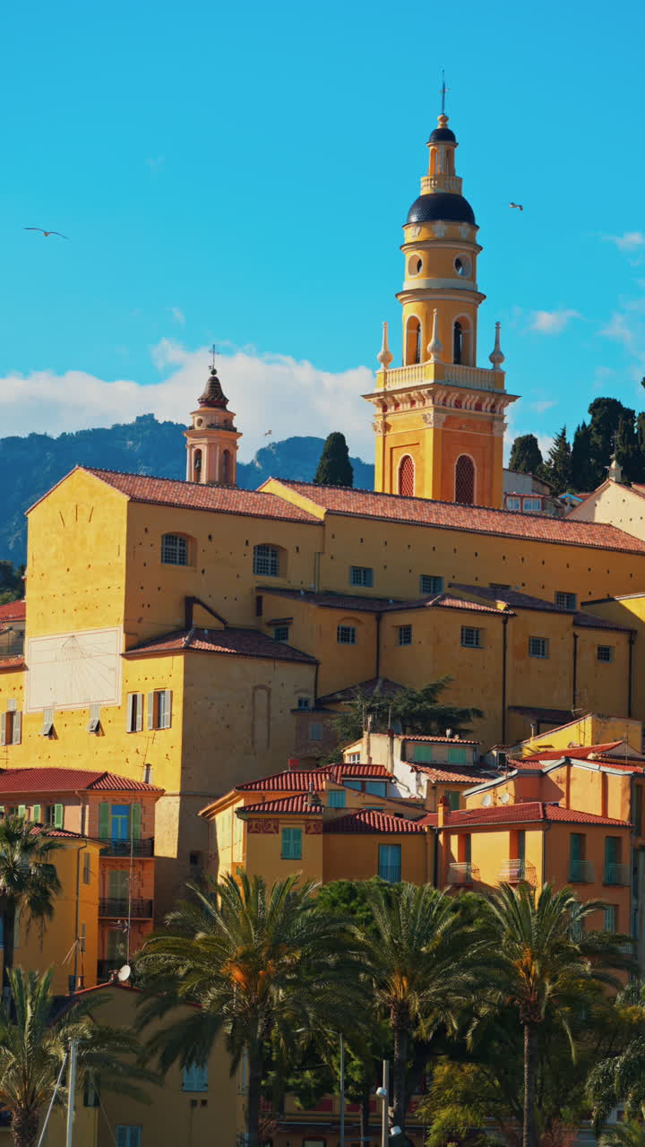 Distant view of the St Michel Basilica surrounded by colourful buildings. Vertical, Menton, France