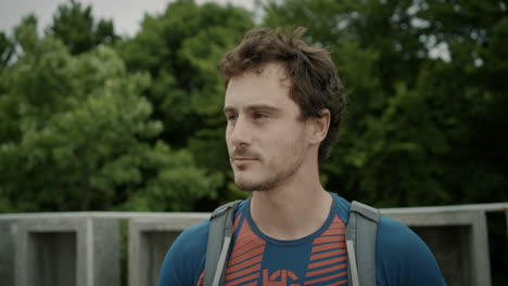 Mid-shot-of-a-young-hiker-with-a-backpack-with-short-brown-hair-taking-a-view-on-top-of-a-tower,-looking-into-the-valley