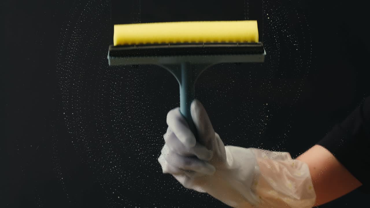 Mano nella mano che pulisce la superficie di vetro con tergivetro e spugna