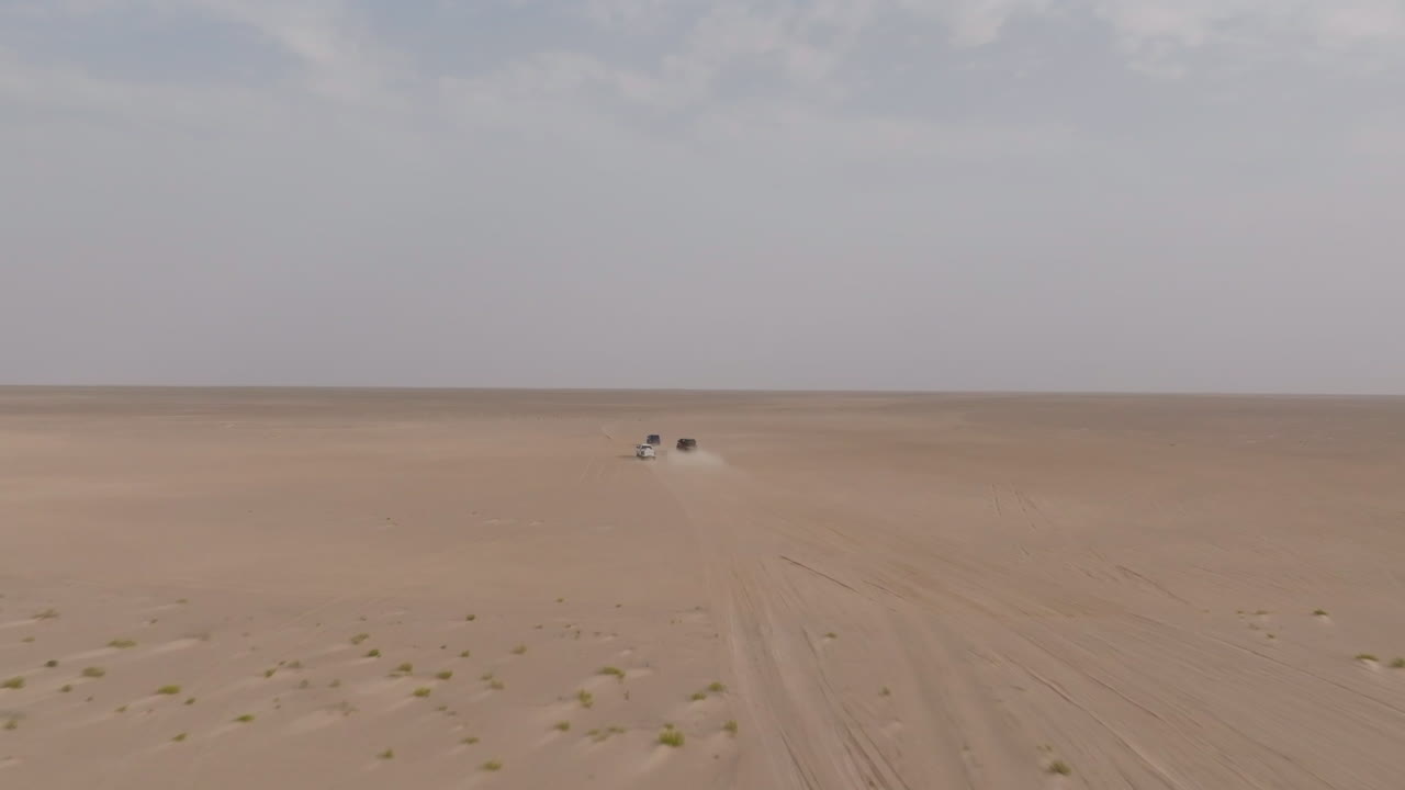 Two off-road vehicles driving across vast desert to Bar Al Hikman, Oman under hazy sky