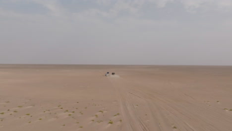 two off-road vehicles driving across vast desert to bar al hikman, oman under hazy sky