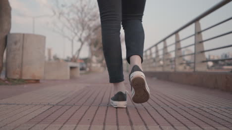 a steady close up shot of a woman's legs and feet from behind as she walks along an empty path