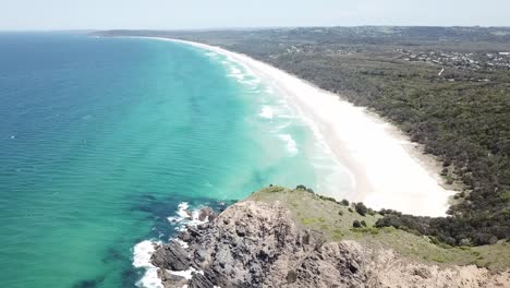 Drohnenschwenk-Hinunter-Zum-Wunderschönen-Blauen-Strand-Mit-Wellen-Und-Weißem-Sand-In-Der-Nähe-Der-Klippe