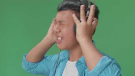 Side View Of Young Asian Boy Listening To Music With Headphones And Dancing In The Green Screen Studio
