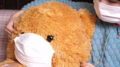 young caucasian girl puts mask on cute teddy bear, covil-19 quarantine