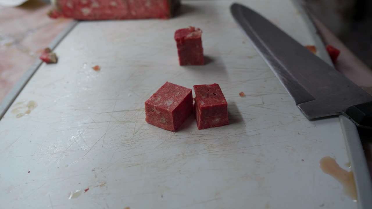 Frossent oksekød skæres i små terninger til madlavning i et køkken.