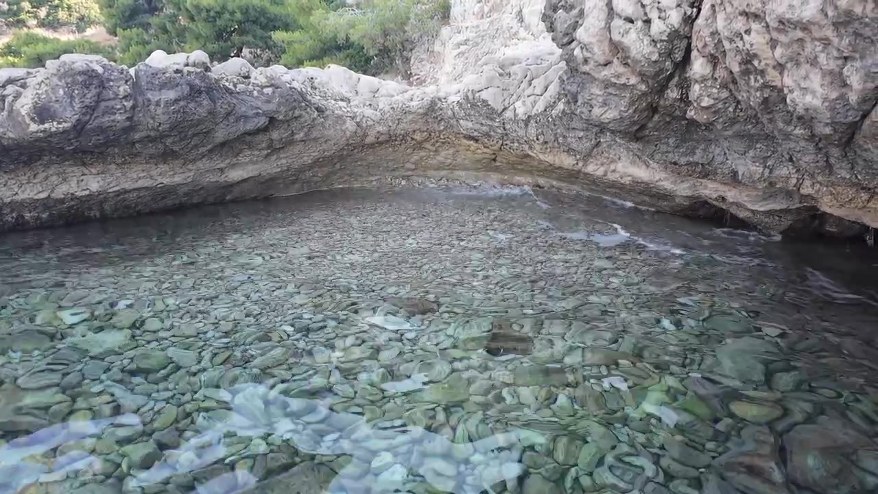 Pittoresca spiaggia rocciosa mediterranea con acqua cristallina turchese e un'atmosfera costiera tranquilla, ideale per viaggi estivi, natura, relax e concetti di vacanza.