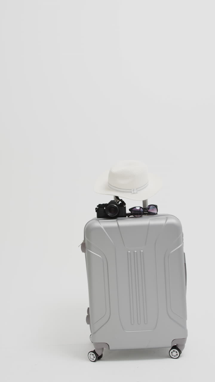 Video verticale di una valigia, macchina fotografica, occhiali da sole e cappello da sole con spazio per il testo su sfondo bianco.