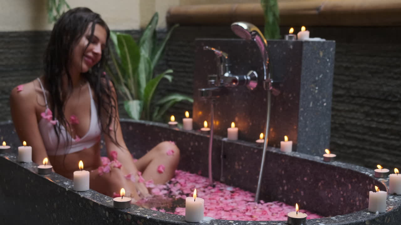 женщина наслаждается романтической ванной со свечами и лепестками розы.