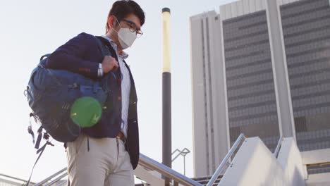 asian man wearing face mask with backpack walking down the stairs at corporate park