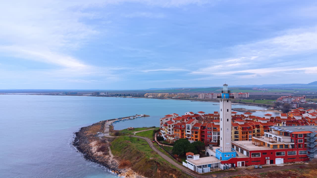 Vista dall'alto di una località balneare con un faro bianco. Borgo costiero con tetti rossi e un'alta torre faro bianca in riva al calmo mare turchese.