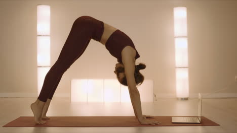 girl doing childs pose in yoga studio. woman looking video on laptop computer