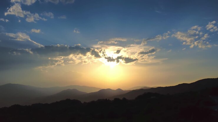 Atardecer dorado sobre colinas onduladas cerca del lago Butrinto, Albania. Un camino sinuoso se adentra en el paisaje mientras una luz cálida atraviesa nubes dispersas, creando una escena vespertina serena y dramática.