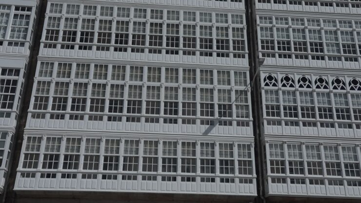 Uma fachada de edifício com fileiras de janelas com moldura branca, fotografada de uma perspectiva frontal.