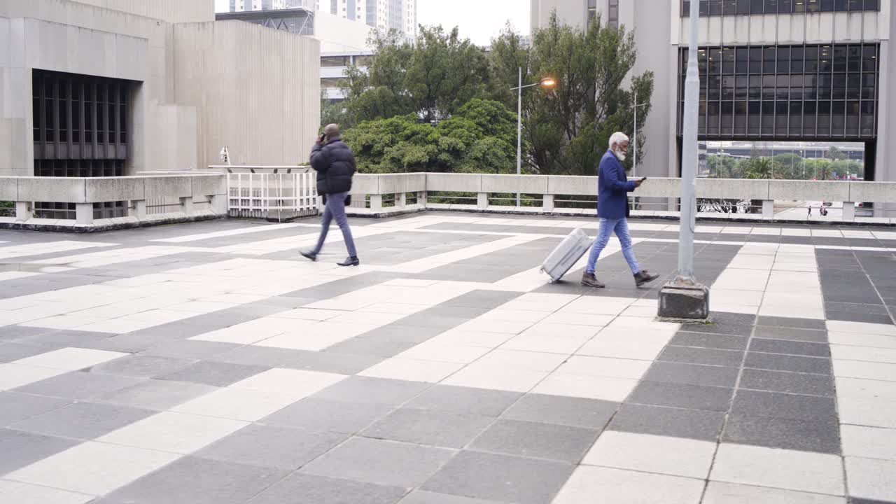 Eldre afroamerikanske menn går inn på en takterrasse, drar en koffert og snakker i telefonen.