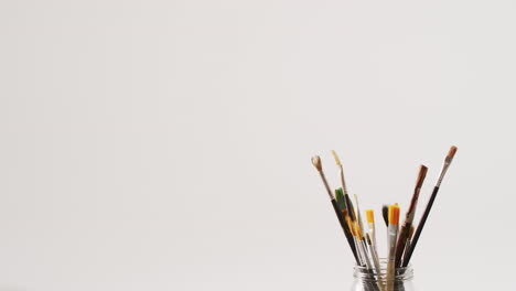 video of a collection of paintbrushes standing in a jar on white background with copy space