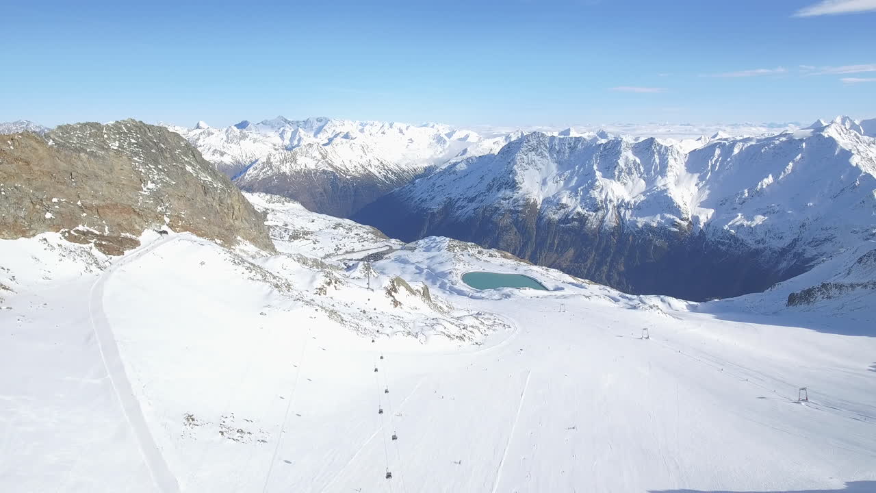 Drone che si muove all'indietro, di fronte a una pista da sci e a un bacino idrico montano in alta quota nelle Alpi di Sölden, Austria, durante l'inverno