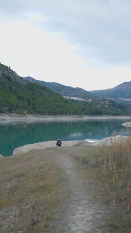 Person sitting by a lake in a mountainous landscape