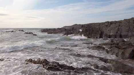 right to left pan of waves crashing against a rocky cove on a summer’s evening in slow motion