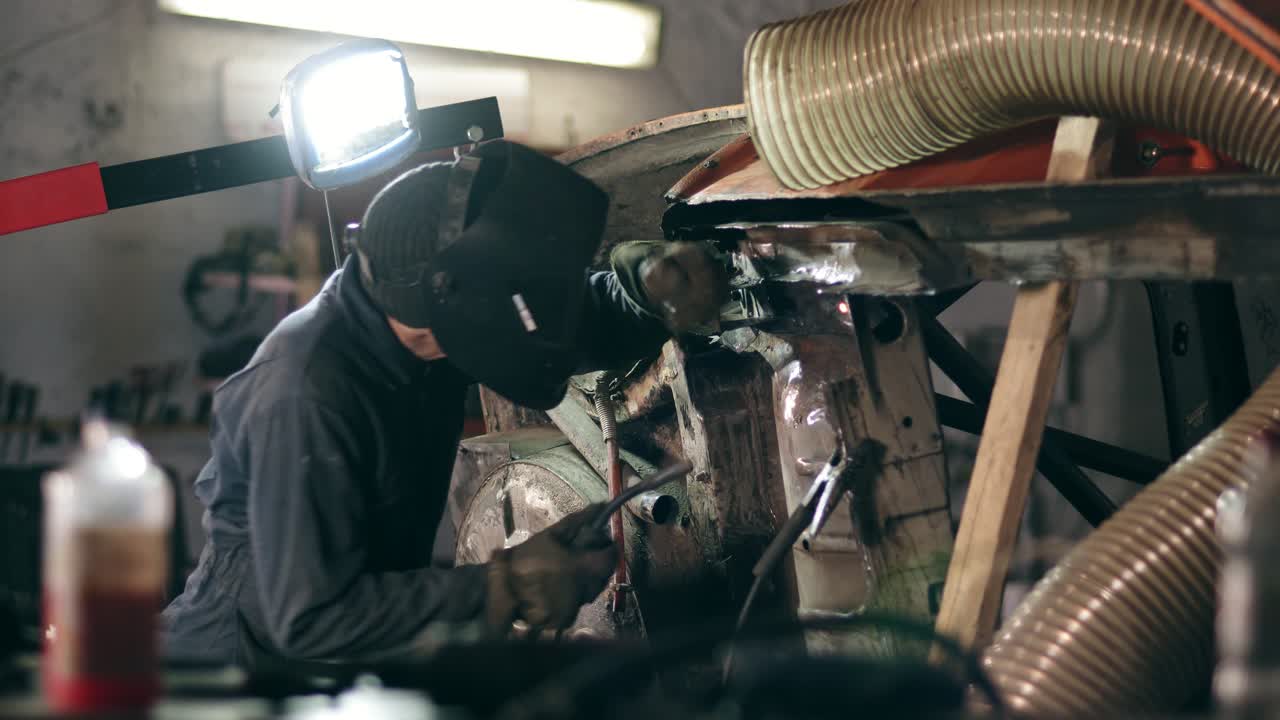 Male worker at a welding factory in a welding mask is working with metal construction. Welding on an industrial plant. Slow motion.