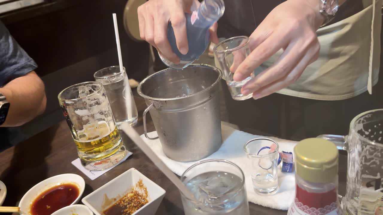 Servitören kyler blå sake-flaska i ishink och häller upp i glas mitt bland vanliga restaurangdrycker